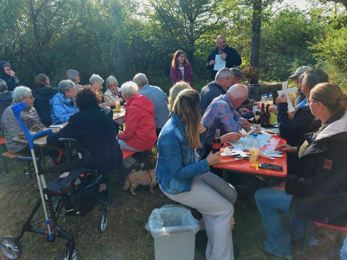 Blick auf eine Gruppe von Menschen. Sie sitzen an zwei Biertischen im Freien.